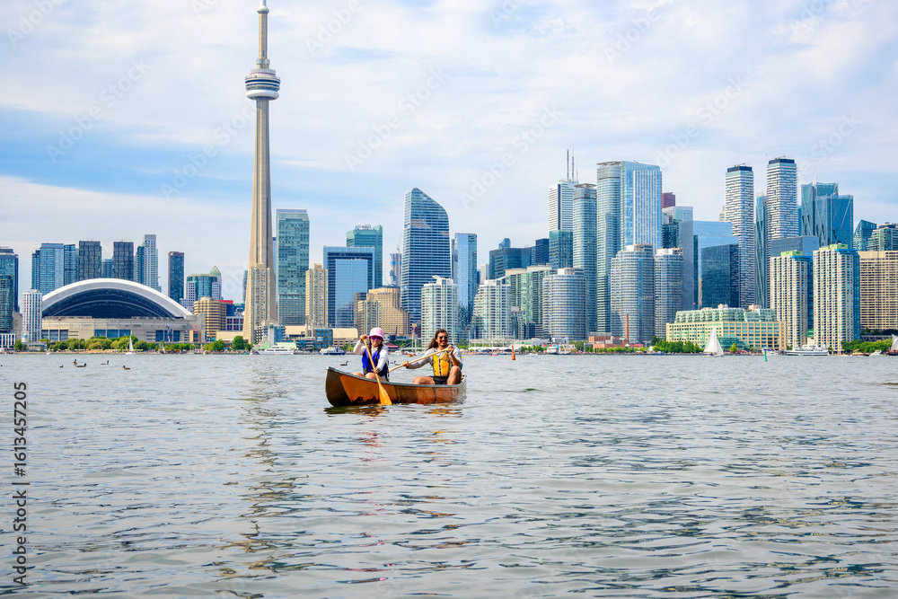 Fototapeta premium Active outdoor lifestyle: young adult couple paddling a canoe on the Toronto Islands in summer with the downtown city skyline in the background room for text copy space