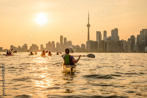 Group of kayakers paddling  into the setting sun and toward the downtown city skyline shot in toronto in summer room for text copy space