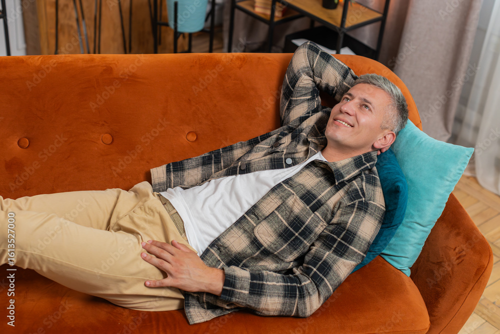 Fototapeta premium Tired young man with gray hair sitting on comfortable couch, taking a rest, daytime nap. Portrait of carefree Caucasian guy relaxing, resting, falling asleep at home apartment in living room on sofa