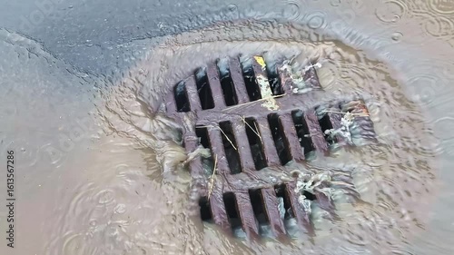 Iron street drain grate with dirty stormwater flowing during rainfall in urban area