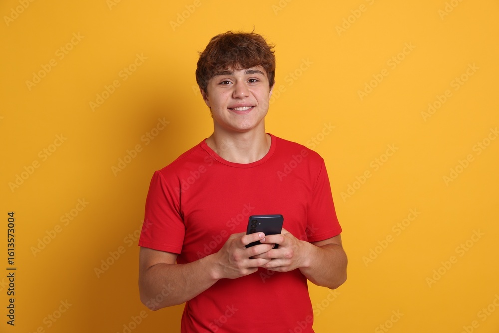 Fototapeta premium Portrait of smiling teenage boy with smartphone on yellow background