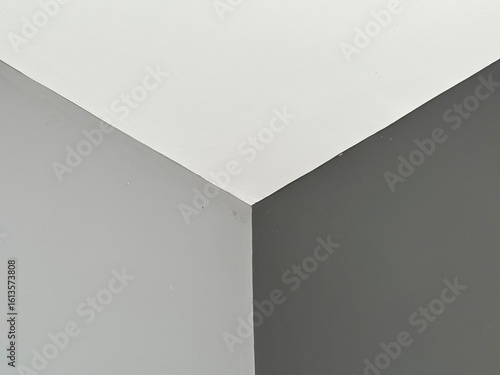 Minimalist interior corner with white ceiling meeting light-grey and dark-grey walls, creating a clean geometric composition and monochrome contrast.