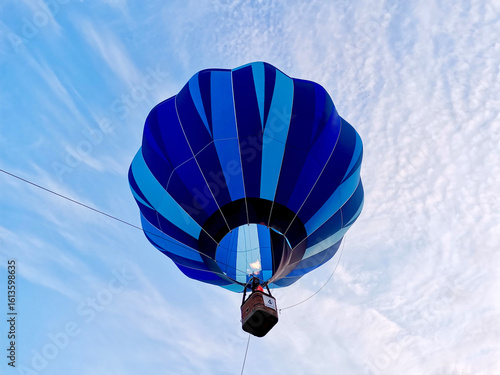 Colorful blue hot air balloon rising into the sky during a summer festival. Clear blue sky.  View from under the balloon