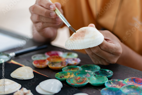 Teenager decorating seashell with paintbrush during art class, creative hobby and craft activity for kids and students.