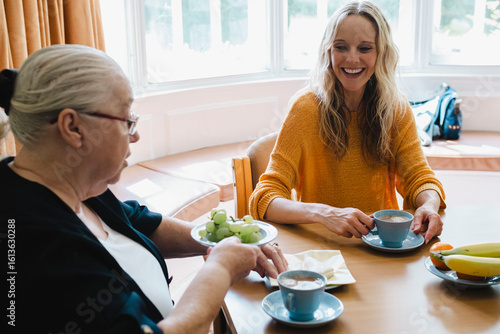 Cheerful caregiver with senior woman having breakfast on table at retirement community
