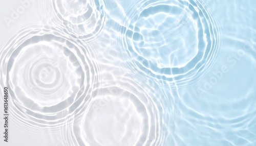 Ripples and concentric circles form on a clear water surface as droplets gently fall, creating soothing patterns and reflections in pale blue hues.