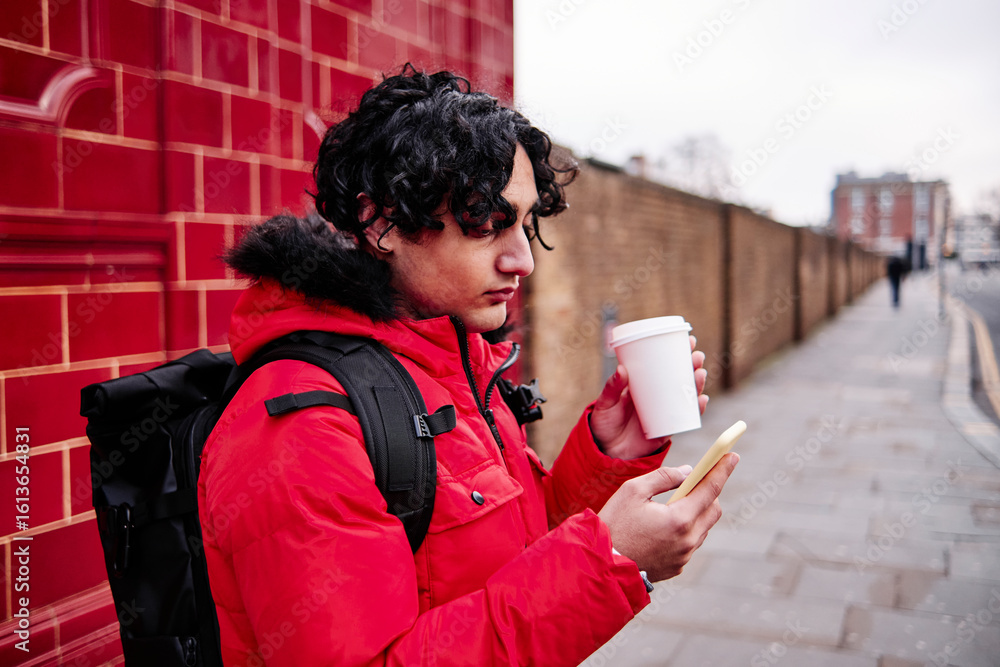 Young man using mobile phone while having coffee on footpath Young man using mobile phone while having coffee on footpath