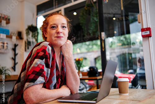 Mid adult woman leaning on table in front of laptop at cafe