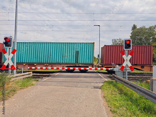Valokuva Train crossing gates blocking road with freight containers passing during daylig