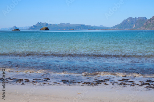 Scenic landscape of Rørvik Beach, featuring striking blue and turquoise waters gently meeting pristine white sand, with majestic mountains rising in the background, Lofoten Islands, Norway