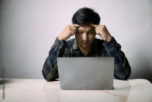 Man deeply focused on laptop, hands on temples, conveying intense thought or stress. Ideal for themes of problem-solving, work pressure, or digital challenges.