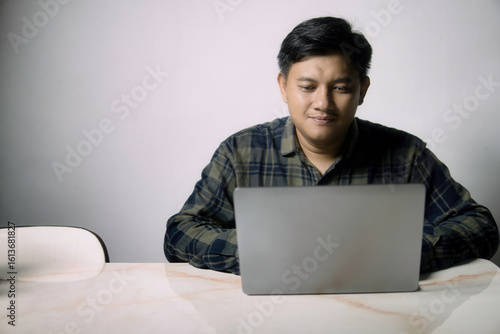 A focused man in a plaid shirt works on his laptop at a table, ideal for remote work, online learning, or digital lifestyle concepts with ample copy space.