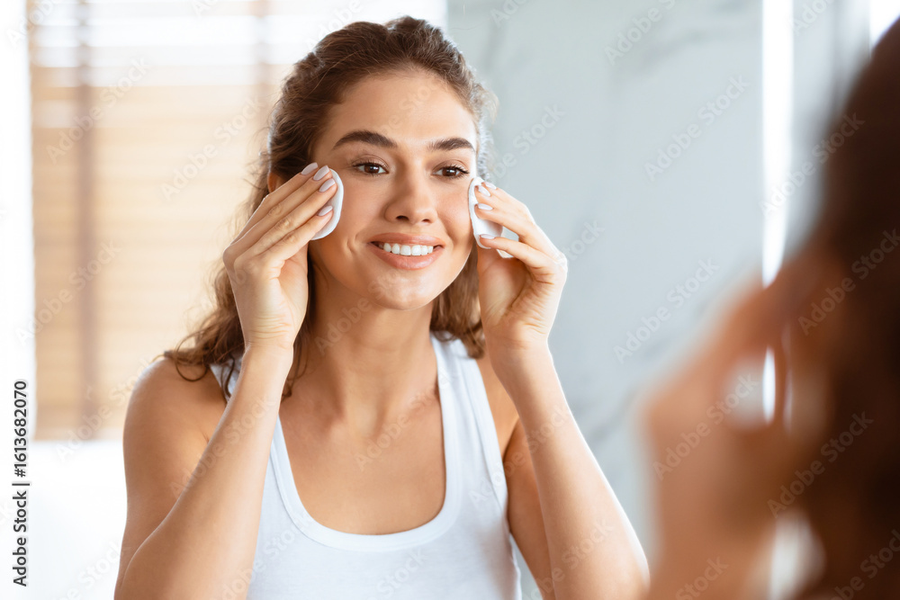 Fototapeta premium Facial Skin Care. Young Woman Using Cotton Pads Removing Makeup And Circles Under Eyes Caring For Face Skin Standing Near Mirror In Bathroom At Home. Skincare Concept. Panorama, Selective Focus