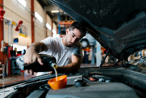 Auto mechanic filling engine oil while standing in garage