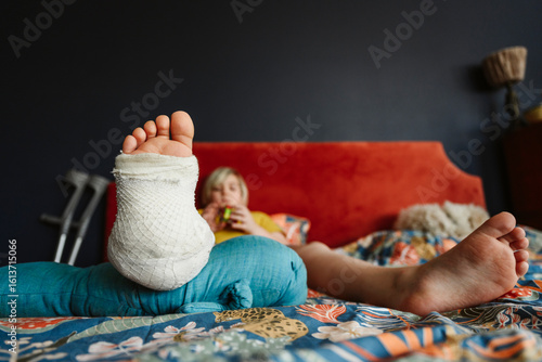 Boy with plaster cast on leg resting on bed at home