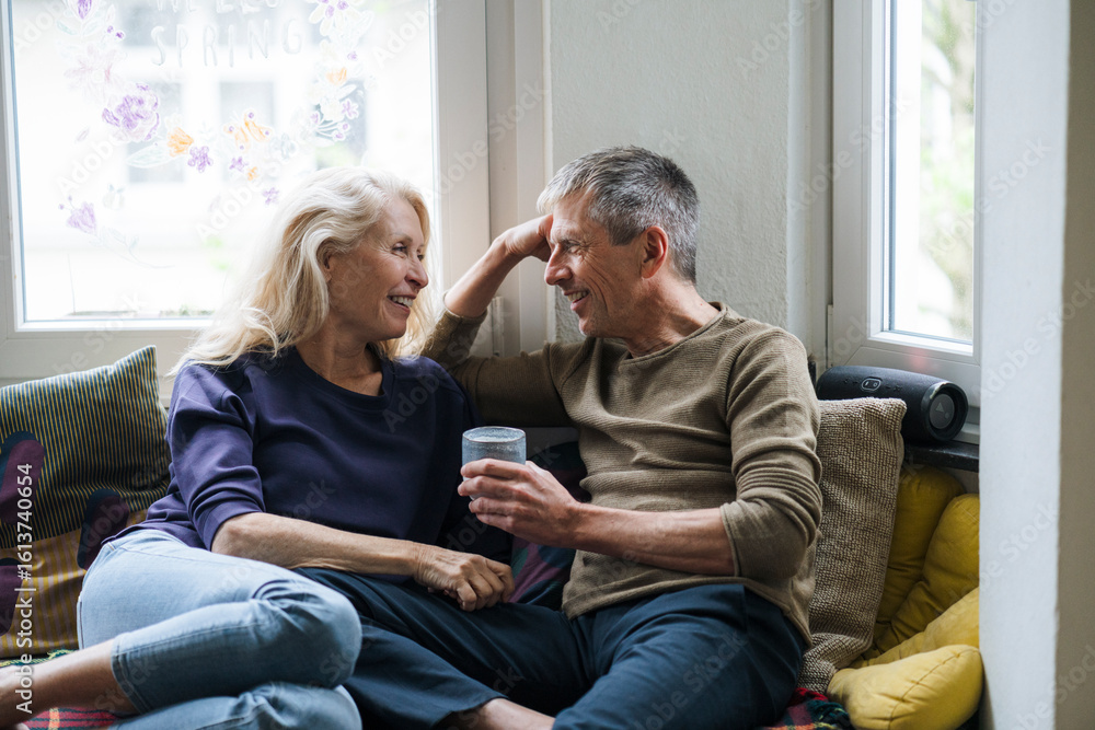 Smiling retired couple sitting on alcove window seat at home Smiling retired couple sitting on alcove window seat at home