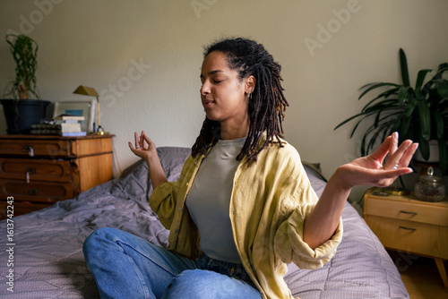 Young woman with braided hair sitting in Mudra position at home