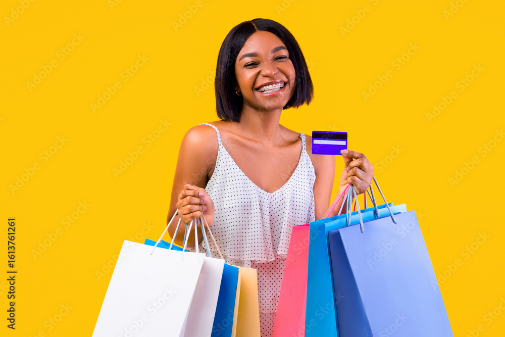 Seasonal shopping concept. Smiling black woman holding gift bags and credit card, smiling at camera on orange studio background. Joyful young lady using electronic money on summer sale Seasonal shopping concept. Smiling black woman holding gift bags and credit card, smiling at camera on orange studio background. Joyful young lady using electronic money on summer sale