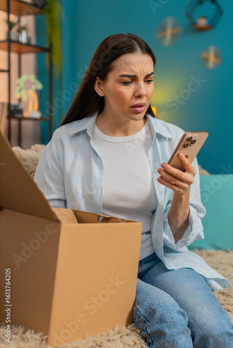 Canvas Print Young woman at home unpacking delivery discovering wrong item, disappointedly in sadness