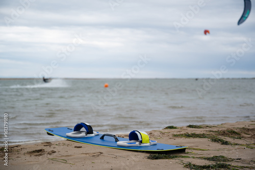 Kitesurfing board lying on sandy beach with kitesurfers riding in background