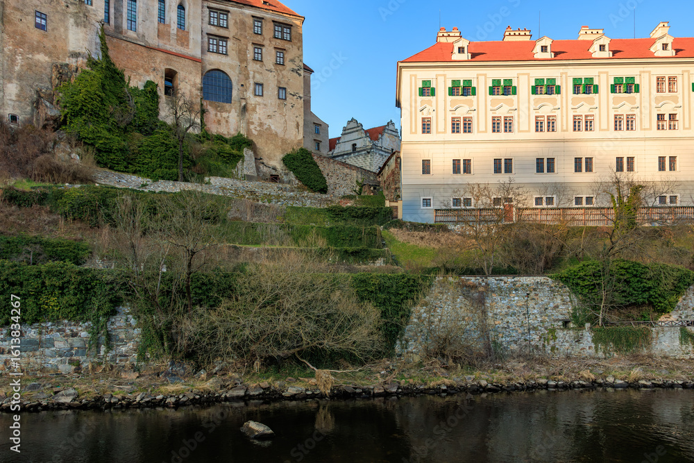 Fototapeta premium Historic czech buildings overlooking riverbank with lush greenery