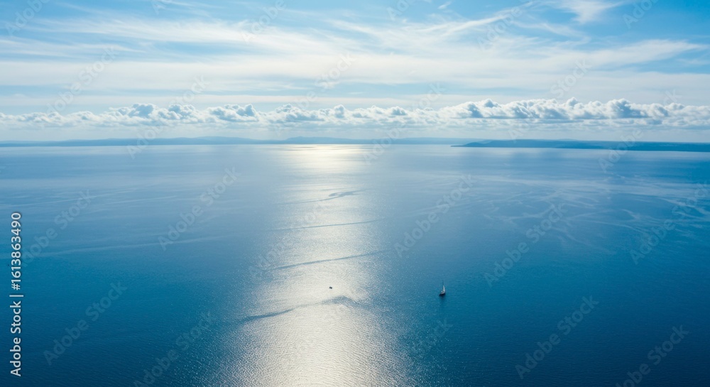 Fototapeta premium Sunlit expanse of serene ocean, a lone sailboat navigating the tranquil waters under a bright sky