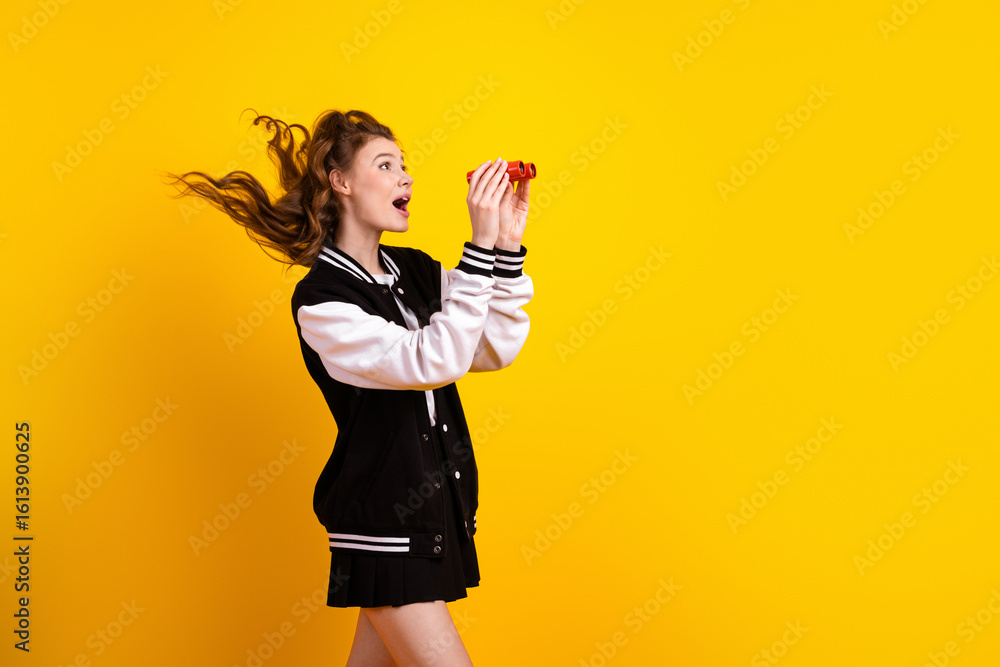 Cheerful young woman in casual sportswear holds binoculars looking forward against a vibrant yellow background Cheerful young woman in casual sportswear holds binoculars looking forward against a vibrant yellow background