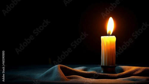 A single candle emits a warm, flickering light, its flame casting shadows in a dimly lit room, evoking a sense of tranquility and contemplation. The candle rests on a soft cloth.