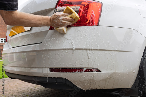 Cuadro en lienzo Person cleaning the rear light of a white car using a yellow sponge and soapy water