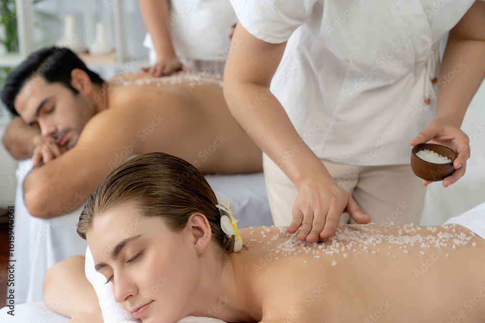 Blissful couple customer having exfoliation treatment in luxury spa salon with warmth candle light ambient. Salt scrub beauty treatment in health spa body scrub. Quiescent Blissful couple customer having exfoliation treatment in luxury spa salon with warmth candle light ambient. Salt scrub beauty treatment in health spa body scrub. Quiescent