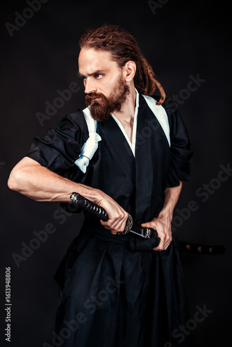 Samurai warrior in traditional Japanese clothing holding a katana sword in a dramatic pose on a dark studio background. Concept of martial arts, Japanese culture, and ancient warriors.