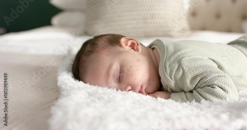 After falling asleep, newborn infant is lying on blanket with cream pillow, breathing gently