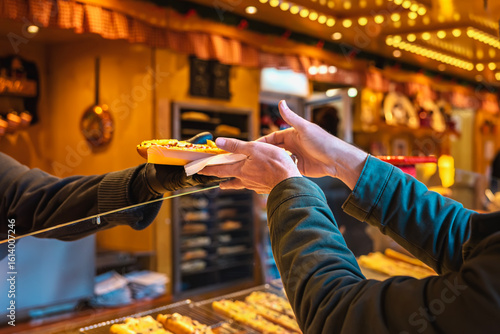 Fototapeta Naklejka Na Ścianę i Meble -  Customer receiving hot food from market vendor over counter at festive food stall, halve of small baguette with cheese and other things. Concept of street food, fast service, culinary interaction