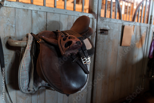 The saddle is hanging on the wall in the stable