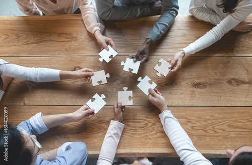 Startup and teamwork concept, top view of creative multiracial team sitting at table and putting together puzzle pieces