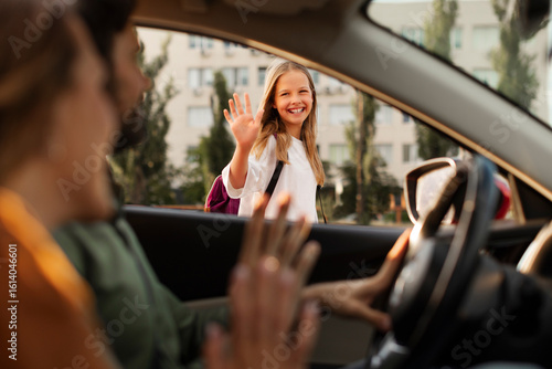 Happy mother and father bringing their daughter to school, sitting in car and smiling, saying goodbye to child girl, view from inside