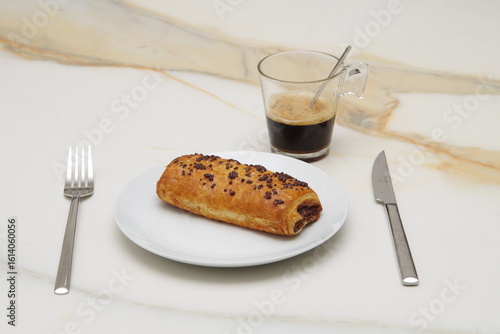 Photos a white plate with a chocolate croissant on a white veined marble background wit