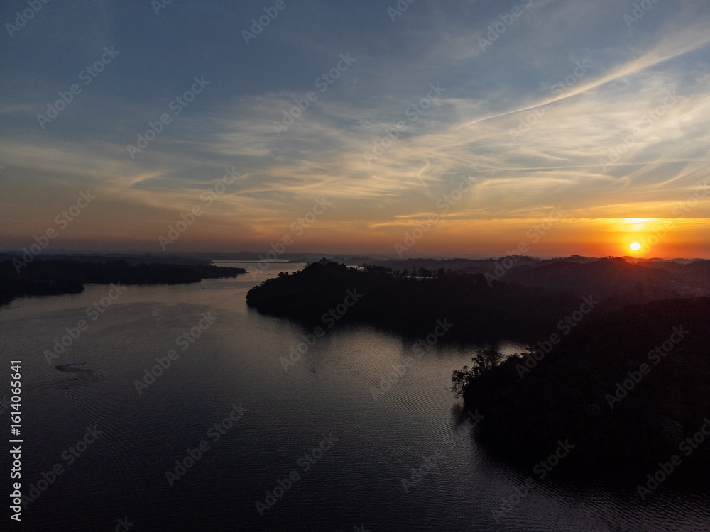 Fototapeta premium Orange sun setting between mountains behind large lake