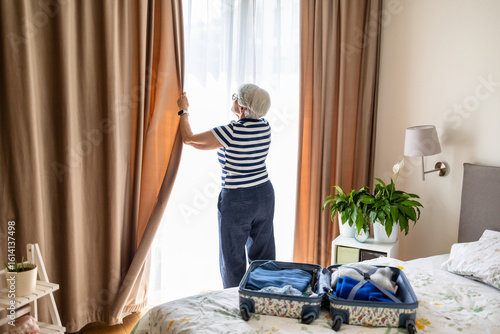 Fotografie Senior woman closing the curtains on a window in a hotel room
