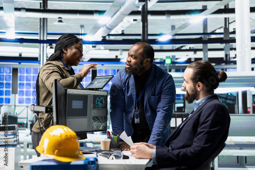 Фотография Multiethnic group of factory engineers in business attire checking equipment and manufacturing processes, showcasing professional teamwork and oversight in solar panel infrastructure