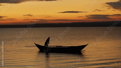 Stunning sunset on lake Victoria and african man standing in boat steers it with long pole pushing off bottom. Concept of silence and pacification