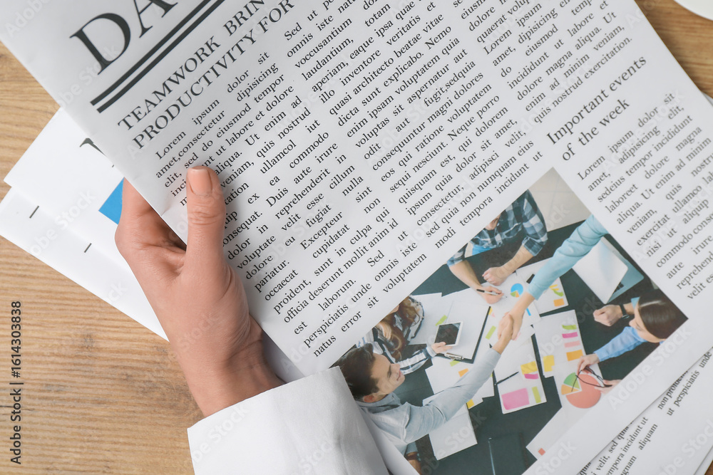 Obraz premium Female hand holding newspaper on wooden background