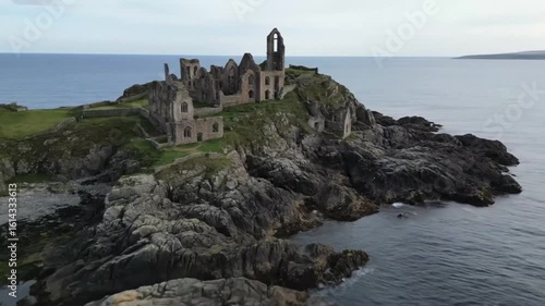 An aerial shot captures the historic peel castle ruins on the isle of man, set against a stunning coastal landscape where the ancient fortress meets the sea