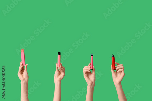 Many hands holding electronic cigarettes on green background