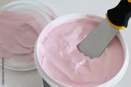 Pink Tinted Joint Compound in a Tub with Spatula