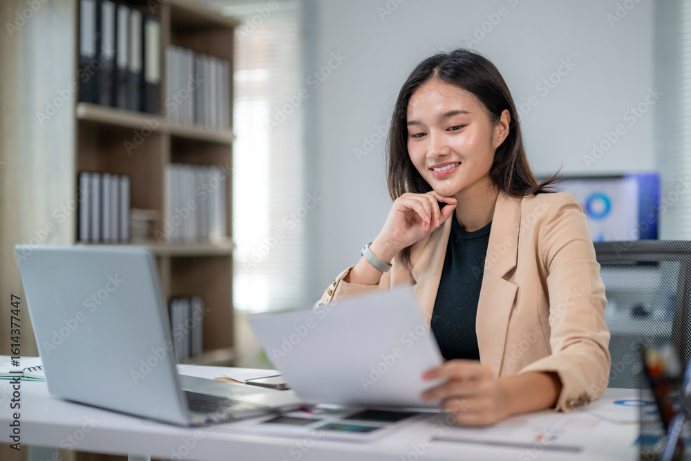 Young asian businesswoman smiling and reading documents at office desk Young asian businesswoman smiling and reading documents at office desk