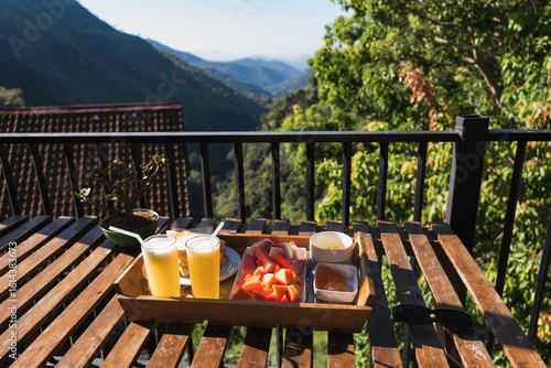 Wooden tray with fresh papaya, watermelon, juice and toasts served for breakfast on balcony with mountain view