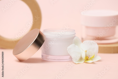 Plaster podiums with jars of cream and orchid flower on beige background