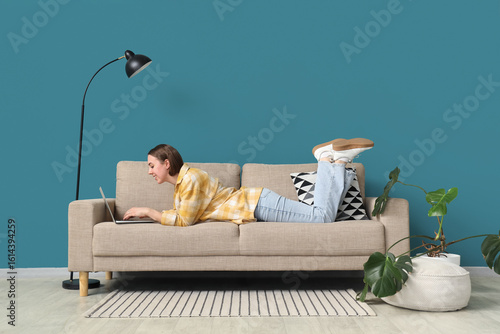 Young woman using laptop on grey couch near blue wall at home