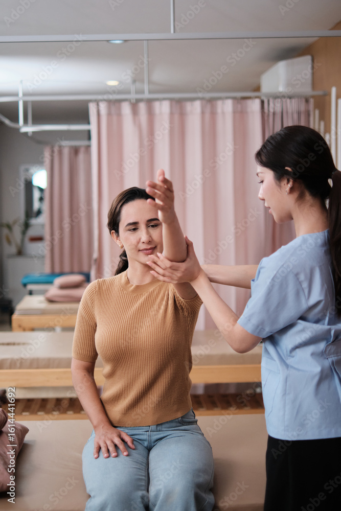 Fototapeta premium Hispanic female patient is arm stretching, treated health recovery, shoulder muscle pain relief by Asian physical therapist doctor, passive medical therapy at healthcare massaging wellness spa clinic.